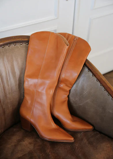 Pair of brown leather knee-high boots on a textured surface with a neutral background