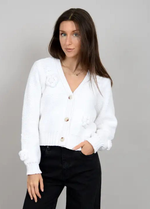 A woman wearing a white long sleeve V-neck cardigan with button-down front over a white top, paired with black pants.